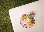Plate with various types of fruit on a beige surface, surrounded by green lawn.