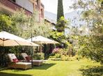 Garden with green lawn, loungers and parasols, surrounded by trees and plants.