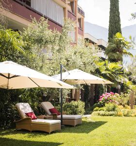 Garten mit grüner Wiese, Liegen und Sonnenschirmen, umgeben von Bäumen und Pflanzen.