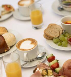 Gedeckter Frühstückstisch mit Cappuccino, Orangensaft und herzhaften und süßen Speisen.