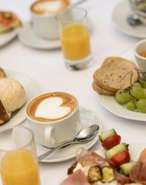 Tavola apparecchiata per la colazione con cappuccino, succo d’arancia e pietanze salate e dolci.