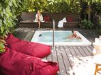 A man relaxes in a hot tub on a wooden terrace, while a woman sits on a bench in the background.
