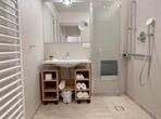 Modernes Badezimmer mit großer bodengleicher Dusche, Waschbecken, Handtuchheizung und hellen Fliesen.