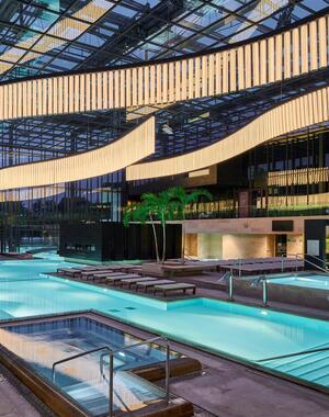 Terme Merano con piscine illuminate, lettini, palme e una grande installazione luminosa sul soffitto.