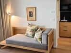 Graues Sofa mit bunten Pölstern, Stehlampe und Blick in die Kochnische.
