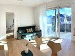 Living area with a wooden table and chairs, sofa and large windows overlooking the balcony.