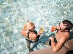 A man and a woman with drinks in the outdoor pool.