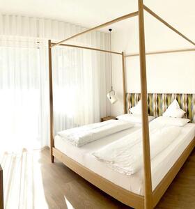 Helles Schlafzimmer mit Doppelbett, Vorhängen, Holzboden und Blick auf den Balkon.