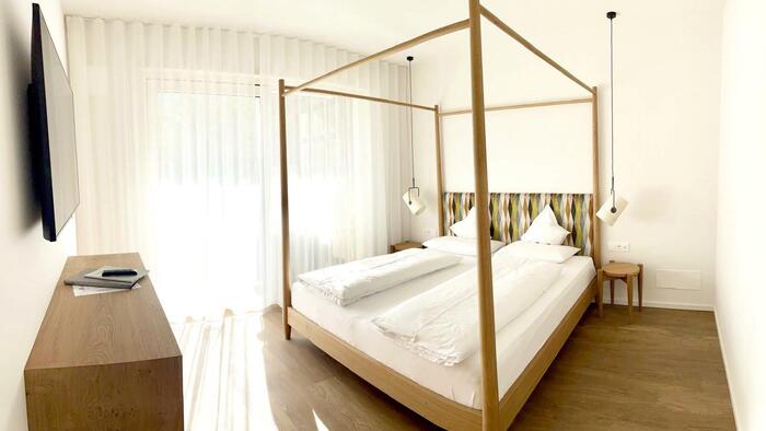 Helles Schlafzimmer mit Doppelbett, Vorhängen, Holzboden und Blick auf den Balkon.