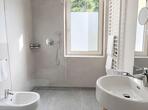 Badezimmer im Apartment Gala mit bodengleicher Dusche, Glasabtrennung, Waschbecken, großem Wandspiegel, WC und Bidet..