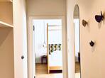 Hallway with wooden flooring, open shelving, an oval wall mirror and a view into the bedroom.
