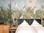 Double bed with white bedding, a green headboard and botanical wallpaper featuring plants and birds at Zea Curtis.