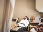 A man in a white bathrobe relaxes on a lounger in the wellness area.