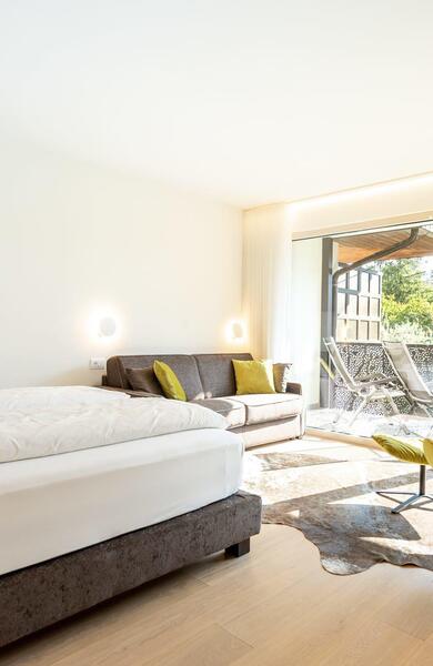 Doppelzimmer mit Doppelbett, grünem Sessel und großen Fenstern mit Blick auf den Balkon.