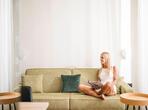 A woman sits on a green sofa at Zea Curtis, relaxing while reading a magazine.
