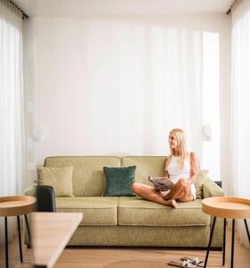 Una donna è seduta su un divano verde allo Zea Curtis e legge una rivista in totale relax.