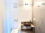 Separates WC im Apartment Palmengarten mit wandhängender Toilette, dunklem Aufsatzwaschbecken und grauer Wand.