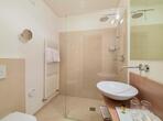 Bagno della camera doppia Pink Lady con lavabo, WC e doccia a filo pavimento con parete divisoria in vetro.