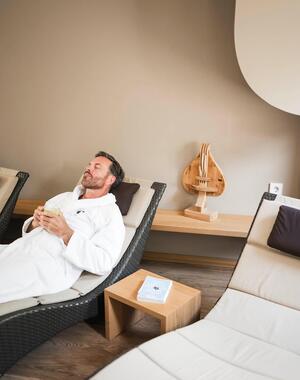 Mann im weißen Bademantel entspannt auf einer Liege im Wellnessbereich.