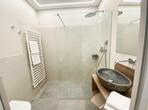Modernes Badezimmer mit bodengleicher Dusche, Waschbecken, WC und hellen Fliesen.