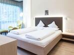 Suite deluxe con letto matrimoniale e testiera imbottita, poltrona verde e lampada da terra accanto all’ampia vetrata.