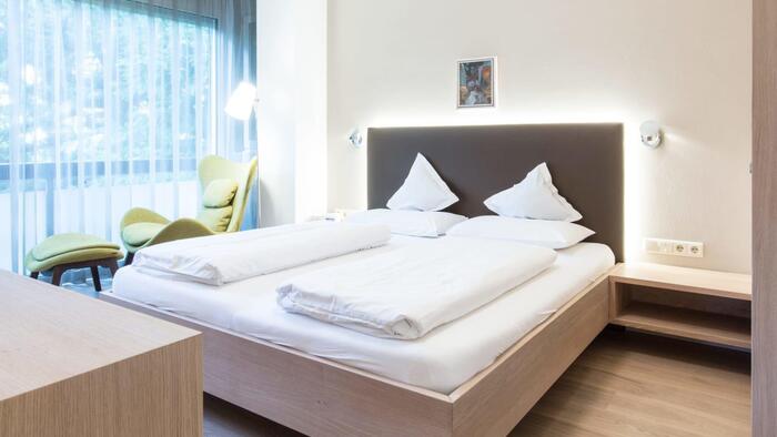 Suite deluxe con letto matrimoniale e testiera imbottita, poltrona verde e lampada da terra accanto all’ampia vetrata.