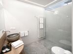 Modernes Badezimmer mit bodengleicher Dusche, Waschbecken, WC und hellen Fiesen.