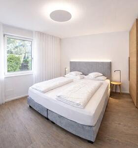 Schlafzimmer im Apartment Gala mit Holzboden, Doppelbett mit gepolstertem Kopfteil, großem Holzschrank, Fernseher und Fenster mit Blick ins Grüne.