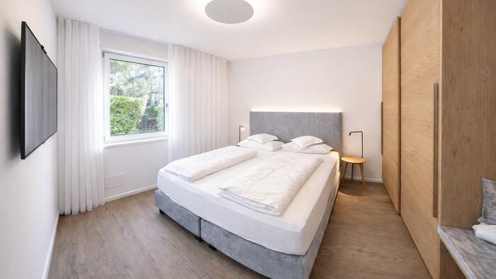 Camera da letto nell’appartamento Gala con pavimento in legno, letto matrimoniale con testiera imbottita, grande armadio in legno, televisore e finestra con vista sul verde.