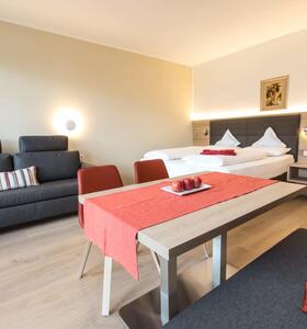 Apartment Pink Lady mit Doppelbett, Essbereich mit Holztisch, grauen Polstermöbeln und grauem Sofa.