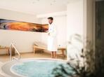A man in a white bathrobe stands beside a hot tub.