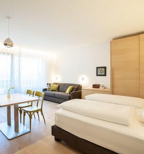 Helles Schlafzimmer mit Doppelbett, Sitzecke, Sofa und Blick auf den Balkon.