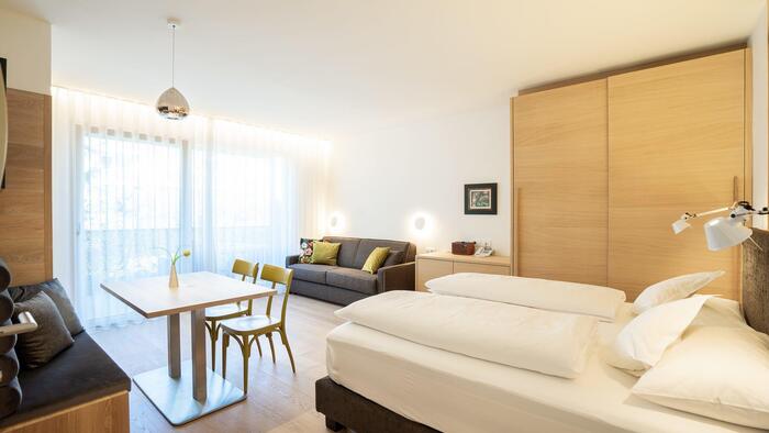 Helles Schlafzimmer mit Doppelbett, Sitzecke, Sofa und Blick auf den Balkon.