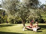 Couple relaxing on loungers in a green garden, surrounded by lawn and trees.