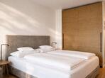 Double bed with an upholstered headboard, bedside lamps and a built-in wardrobe with wooden doors in the Meranderapfel double room.