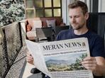 A man reads a newspaper on the balcony.