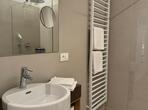Bathroom in the Königapfel deluxe suite with a washbasin on a wooden vanity unit, large wall mirror and level-access shower with a glass partition.