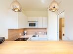 Moderner Essbereich mit Holztisch, Blick auf die Küchenzeile mit weißen Fronten und Holzdetails.