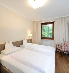 Zimmer im Apartment Palmengarten mit Doppelbett, Fernseher an der Wand, einem Sessel neben dem Fenster mit Blick ins Grüne.