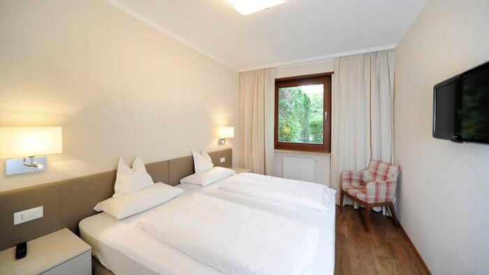 Camera nell’appartamento Palmengarten con letto matrimoniale, televisore a parete e una poltrona accanto alla finestra con vista sul verde.